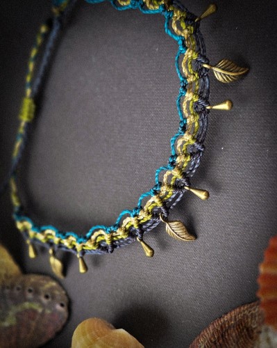Ręcznie pleciona bransoletka na kostkę z mikromakramy wykonana ze sznurka Linhasita w kolorach granatowym, morskim, oliwkowym i złotym. Regulowana biżuteria boho handmade z zawieszkami w kolorze antycznego brązu.